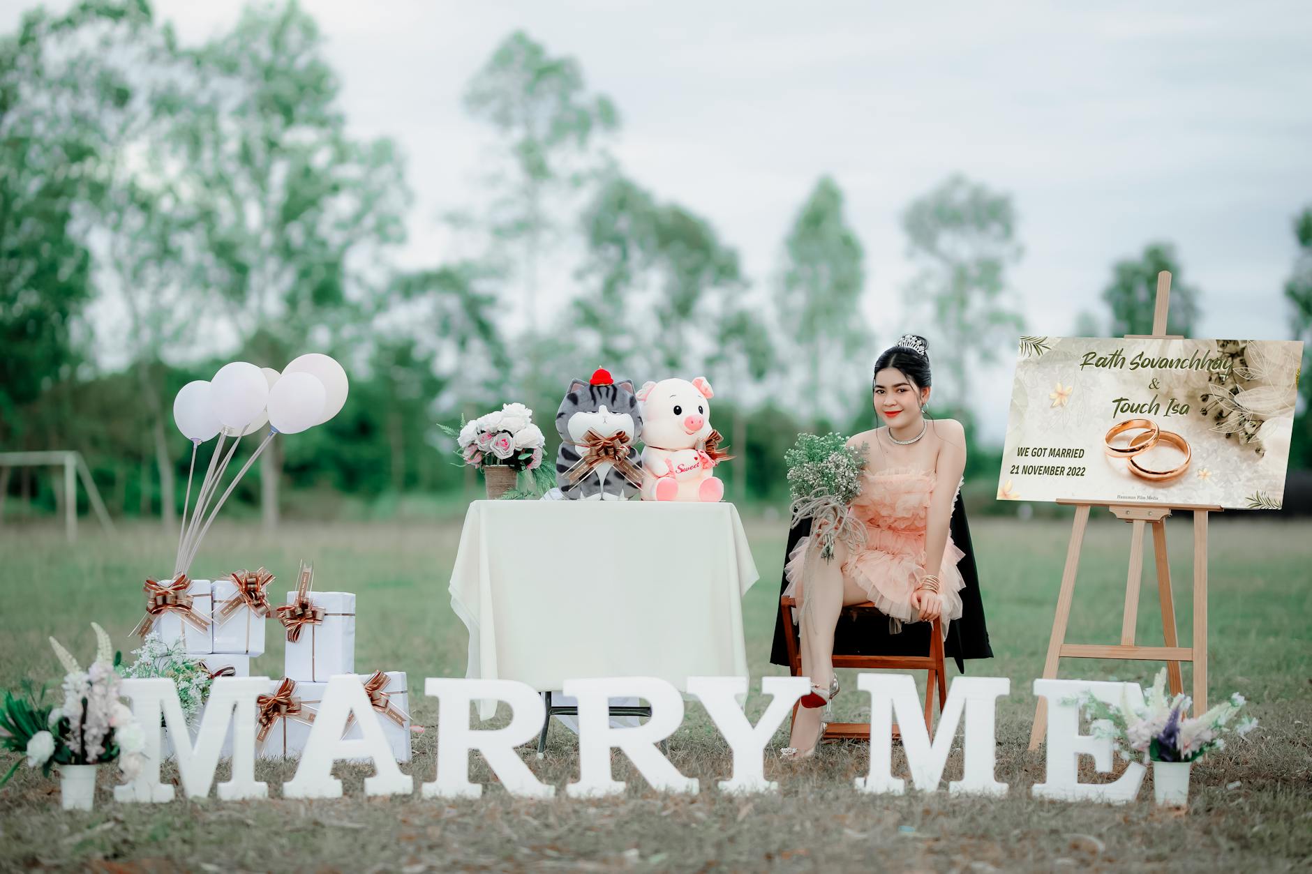 young woman in a pink dress sitting at a table with stuffed animals and marry me sign